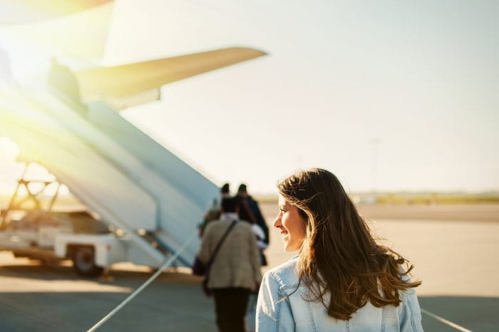 Woman tourist passager getting in to airplane at airport, walking from the terminal to the plane.